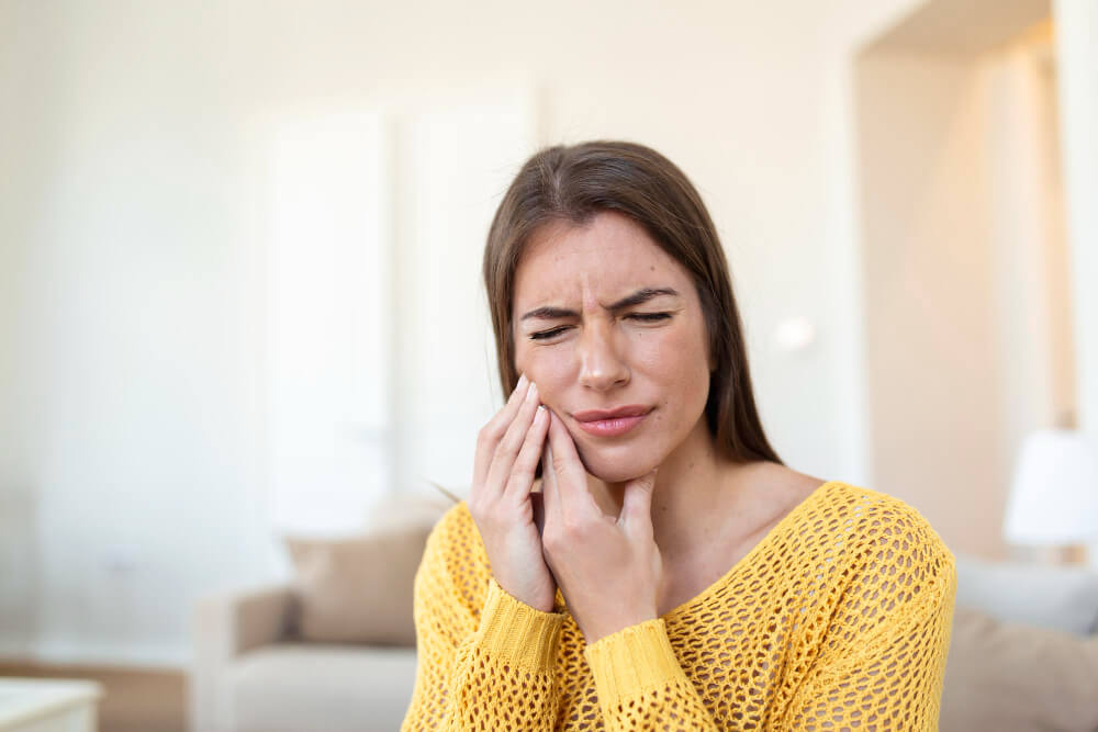 a woman in yellow sweater having a tooth pain
